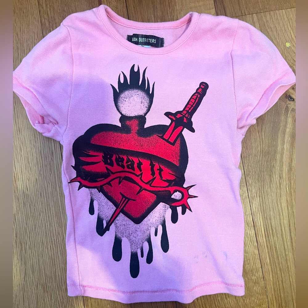 Pink Urban Outfitters baby tee with beat it heart graphic.
